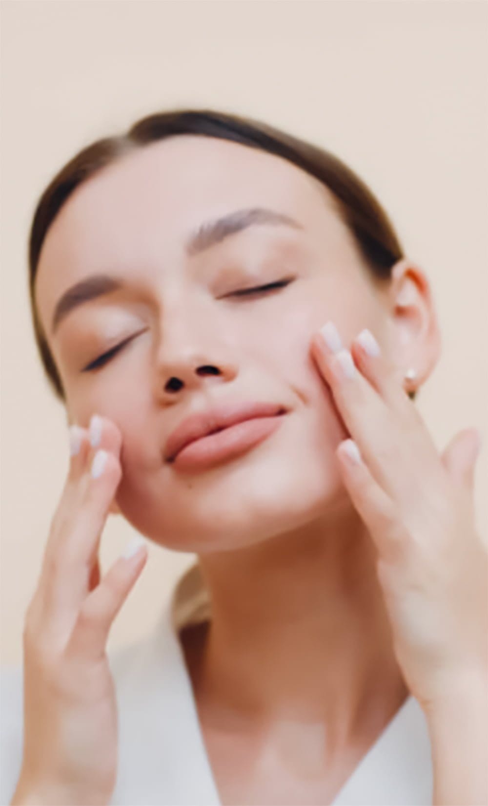 Woman with closed eyes gently touching her face with both hands, appearing relaxed and content.