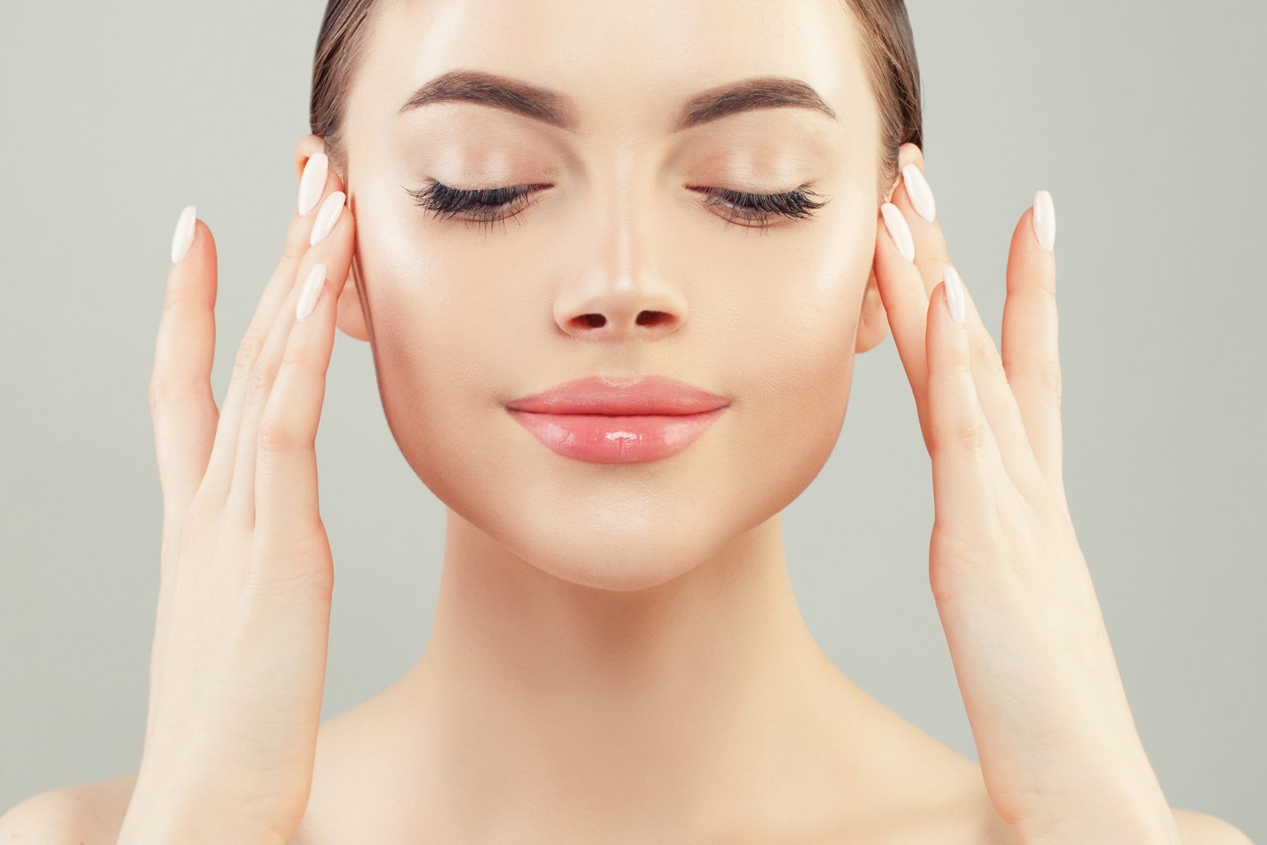 Woman with closed eyes gently touching her face, highlighting clear skin and a serene expression—perfectly capturing the essence of a soothing facial moment.