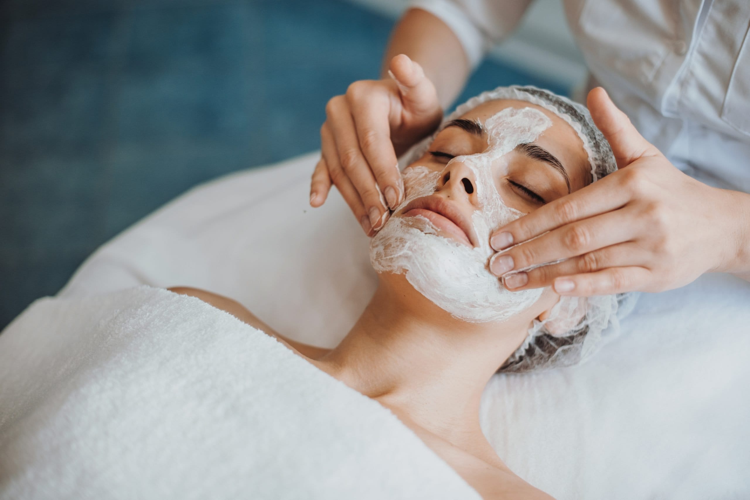 A person enjoys a relaxing spa experience, receiving Facial Treatments as soothing cream is gently massaged onto their face.