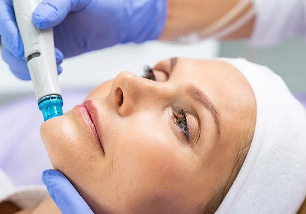 Person receiving a facial treatment with a blue-handled device, wearing a white headband and lying down.