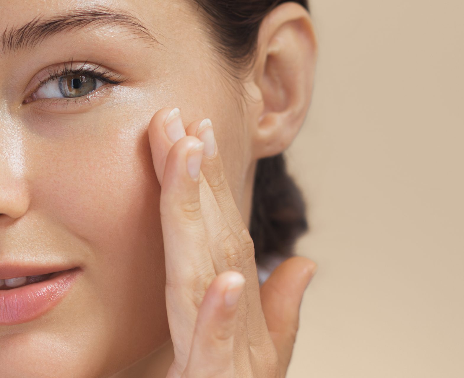 Woman touching her cheek, close-up on face with clear, radiant skin and natural makeup, beige background.