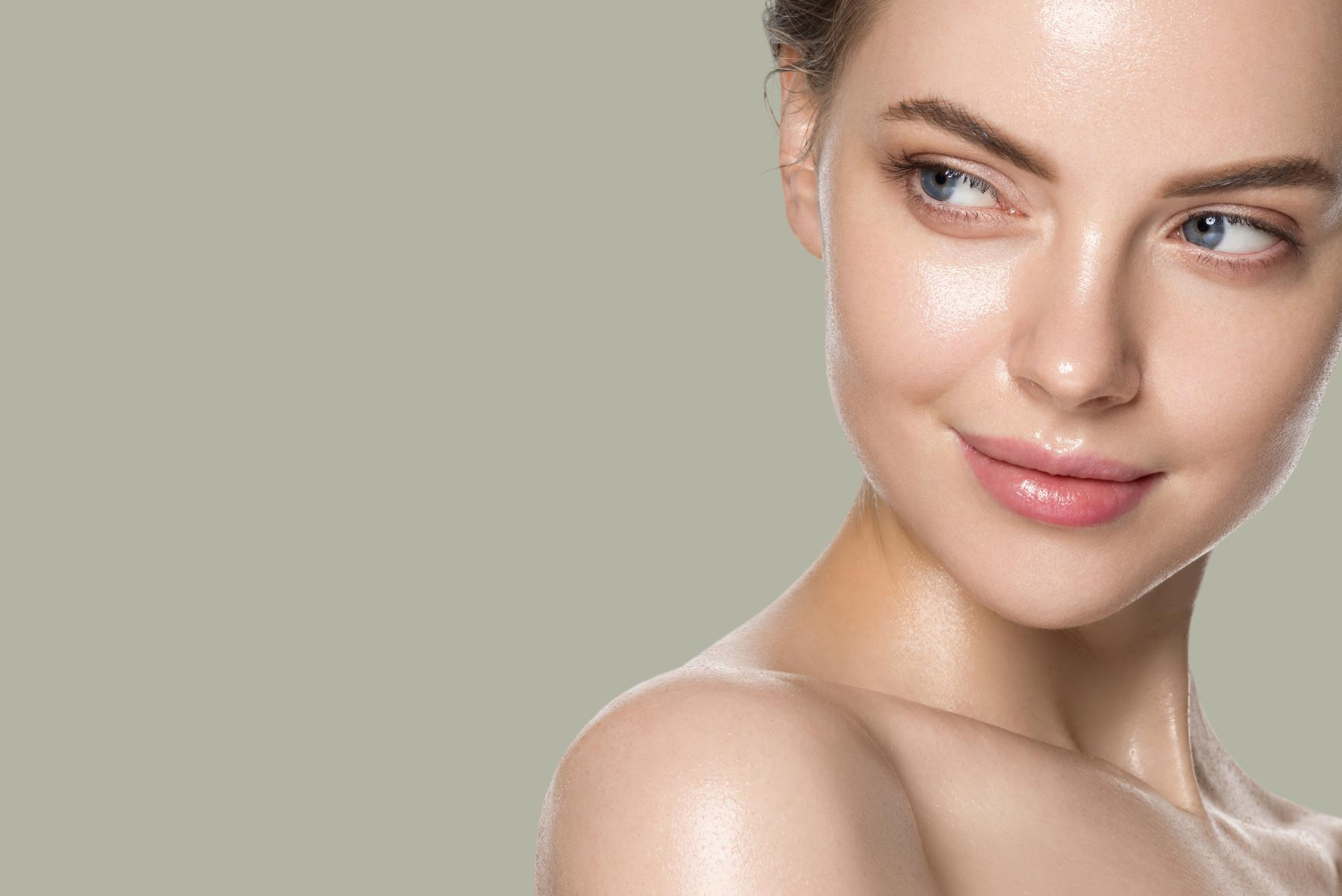Woman with glowing, clear skin looks to the side, smiling gently against a plain light grey background.